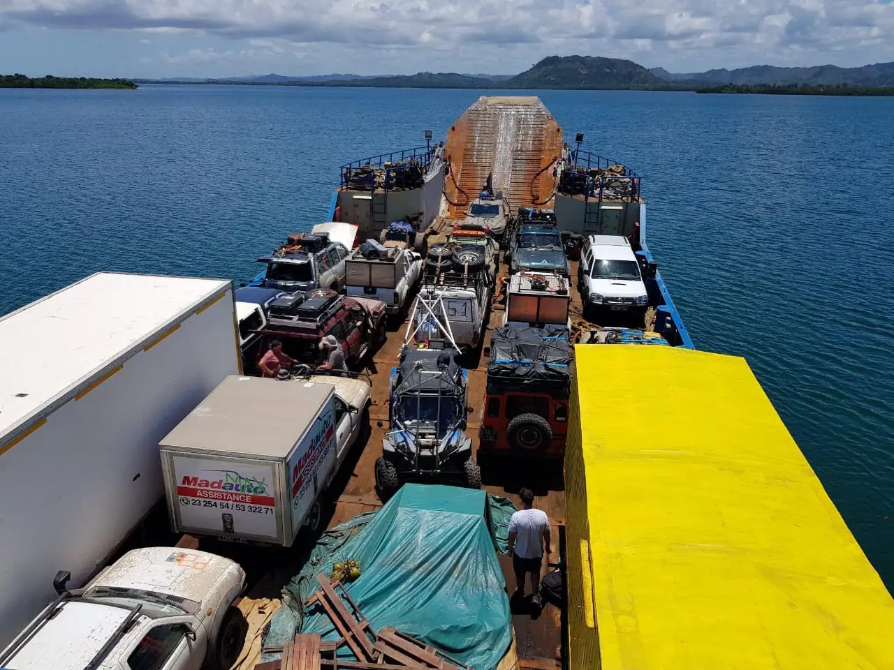 Convoy of production vehicles and trucks crossing a bay on a barge in Madagascar