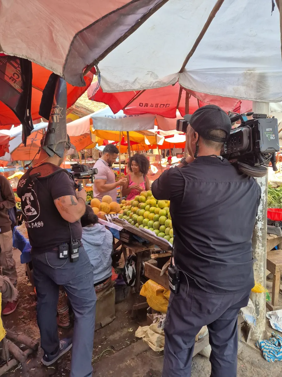 TV crew filming presenters at a fruit stall in a colourful market in Madagascar