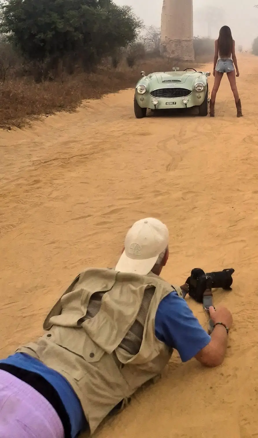 Photographer lying on the sand shooting a model and a vintage roadster on the Avenue of the Baobabs, Madagascar